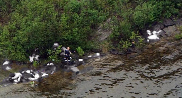 An image taken from a helicopter showing what Norwegian police believes is suspect Anders Behring Breivik (C) carrying a gun, next to several bodies at the Utoya island shore during the 22 July 2011