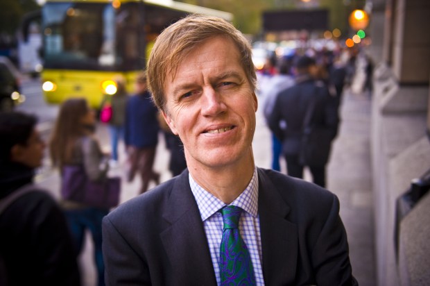 a man in a suit and tie stands in front of a yellow bus