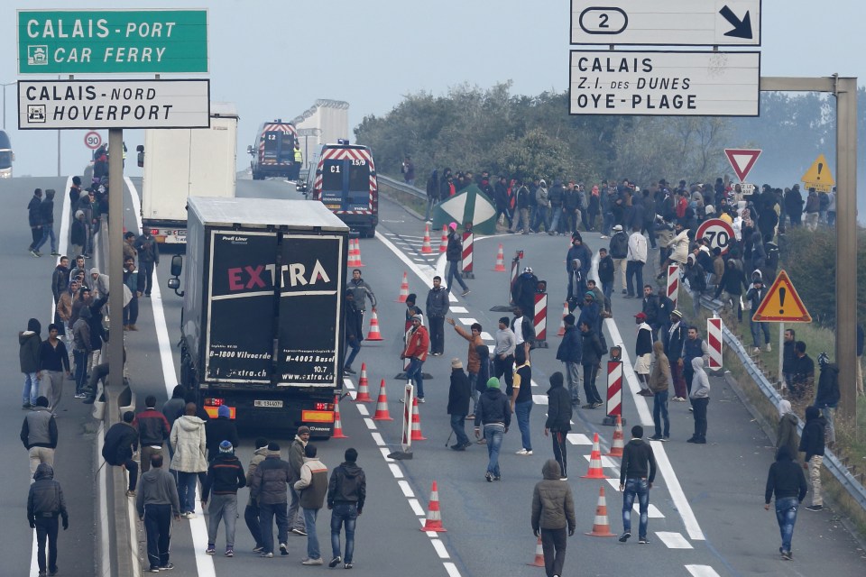 Dozens of migrants gather near lorries which head towards the ferry terminal in Calais