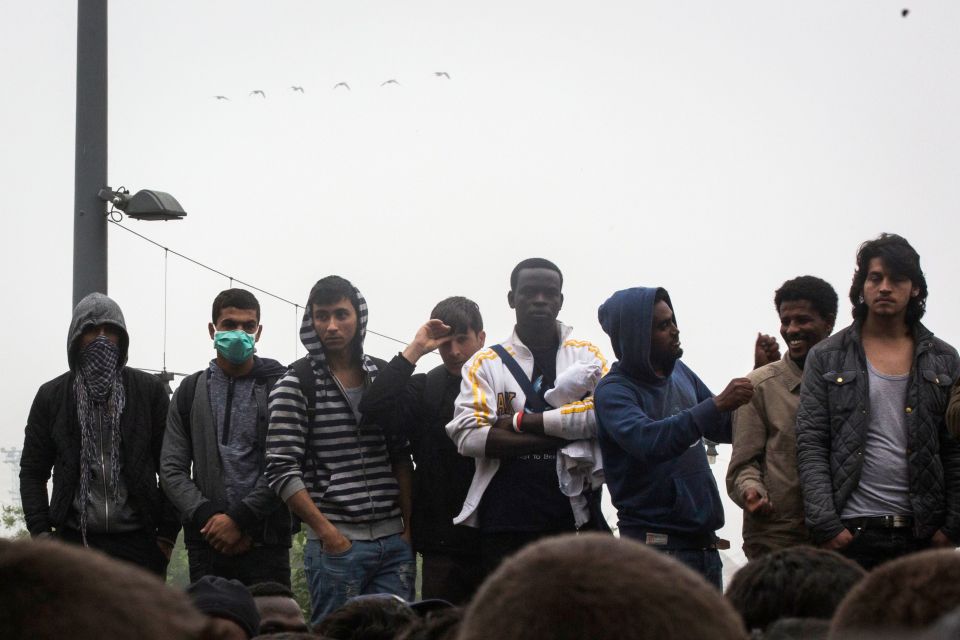 Migrants stand as they wait to board a bus to a new home