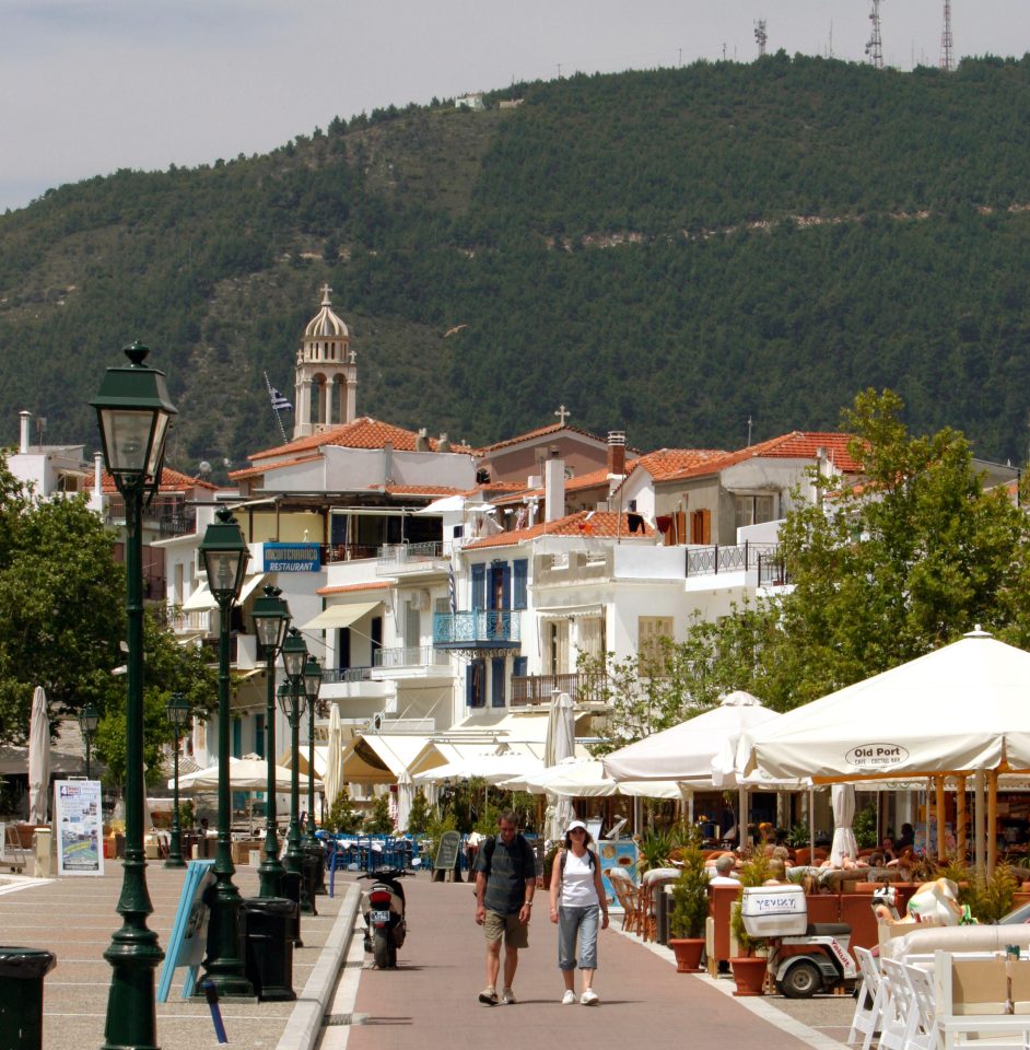  Tourists walking by a streetside cafe in the Old Port of Skiathos town