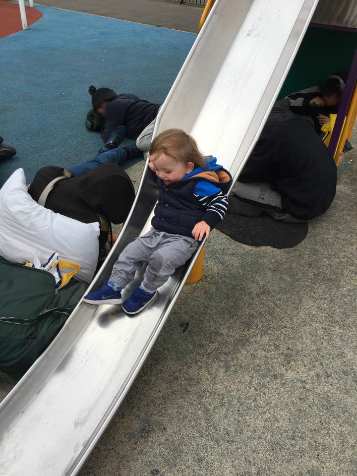  Toddler Devon plays in Green Grosvenor Park, Salford, as men appear passed out beside him