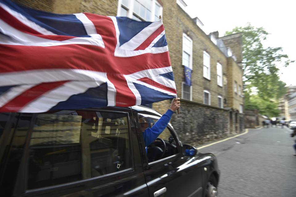 A taxi driver holds a Union flag as he celebrates the vote for Brexit this morning