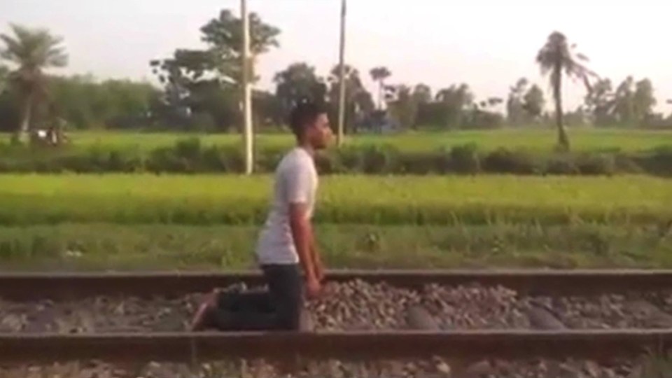 The man kneels on the tracks as the cameraman begins to urge him to lie down