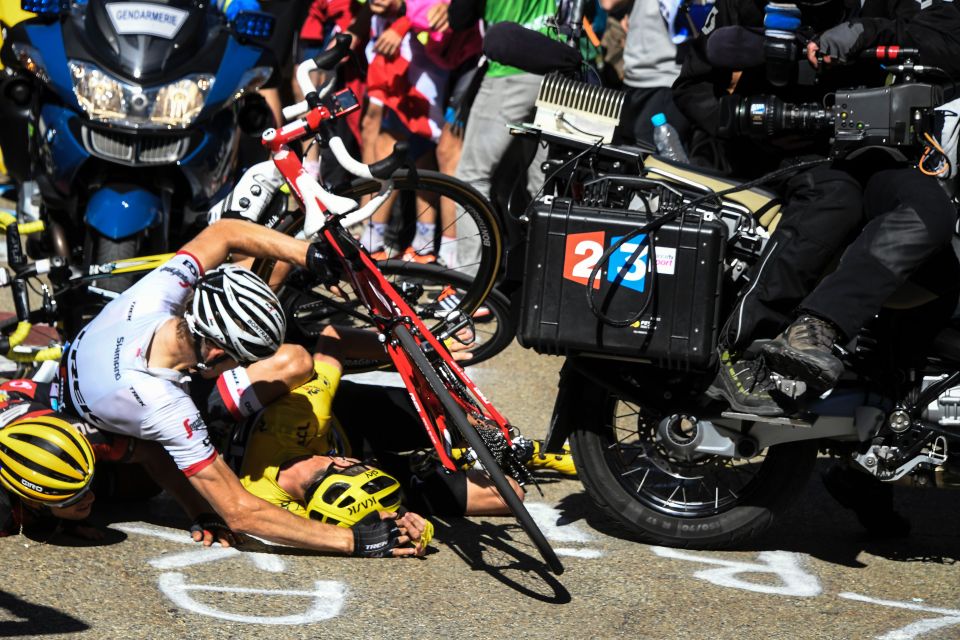 Chris Froome in the yellow Kask helmet is at the bottom of a pile of riders as his bike is broken by an official's motorbike (left)