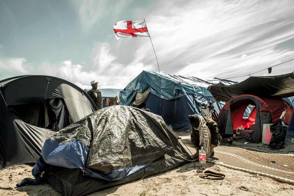 Migrants stand next to a flag of England inside the "Jungle" camp