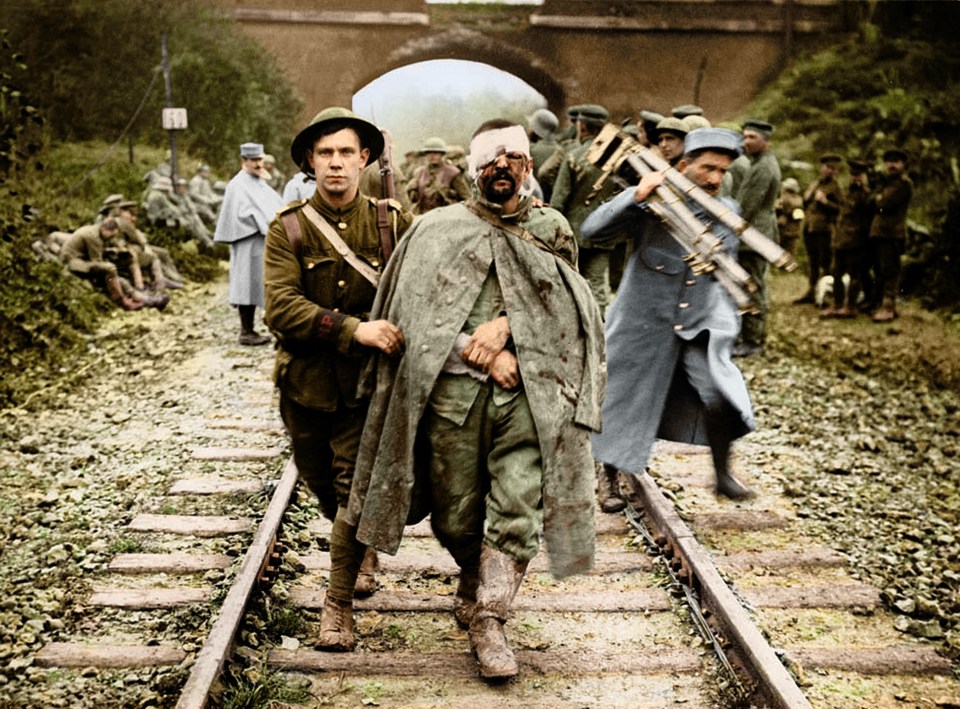  A British soldier helps a wounded German prisoner walk along a railway track