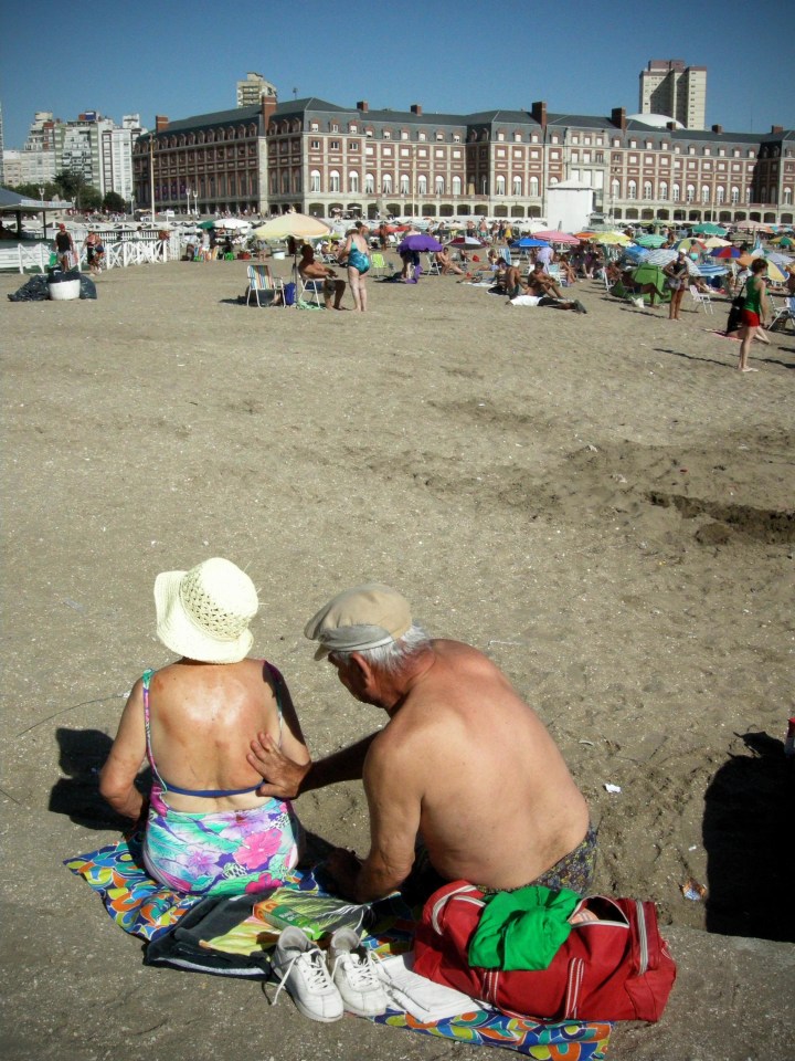 An Elderly Man Spreads Sunscreen On The Back Of A Woman