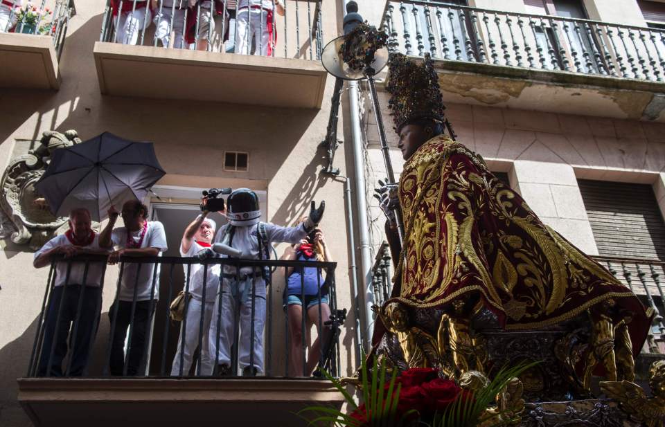  A spectator in an astronaut suit watches from a balcony as the effigy of San Fermin is carried through the centre of Pamplona