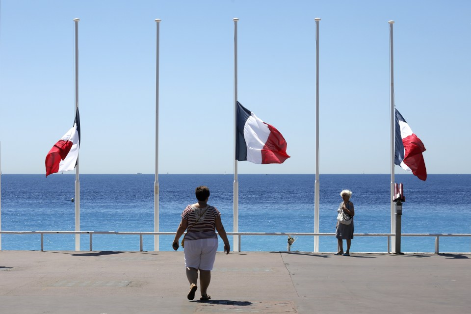 People stroll on the Promenade des Anglais with the French flag at half mast, near the scene of the truck attack