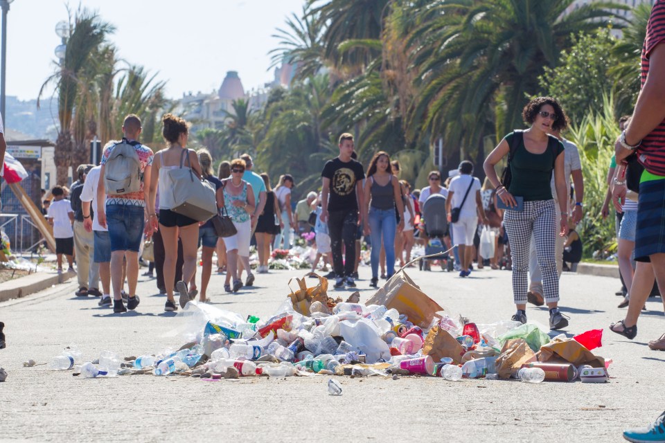  As the Memorial of Hate lies piled with burnt rubbish people carry on with their day along the Promenade des Anglais