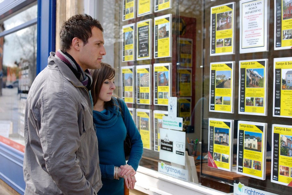 A young couple aspiring to buy their first home browse the listings in an estate agency window