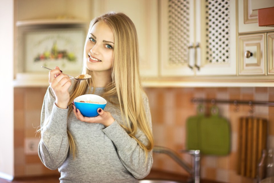 Beautiful blond hair girl eating oatmeal in the kitchen