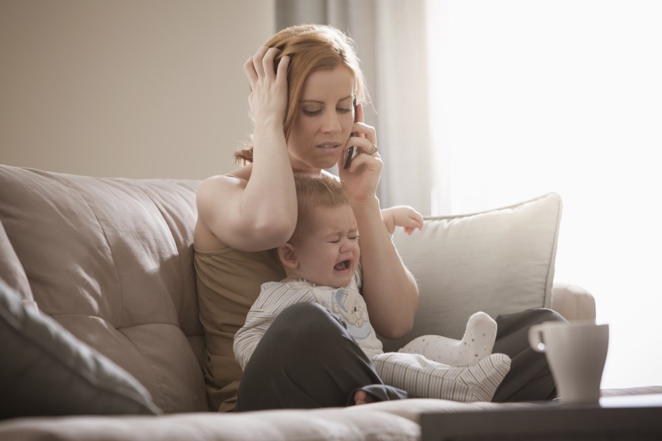 mother holding crying son and talking on cell phone