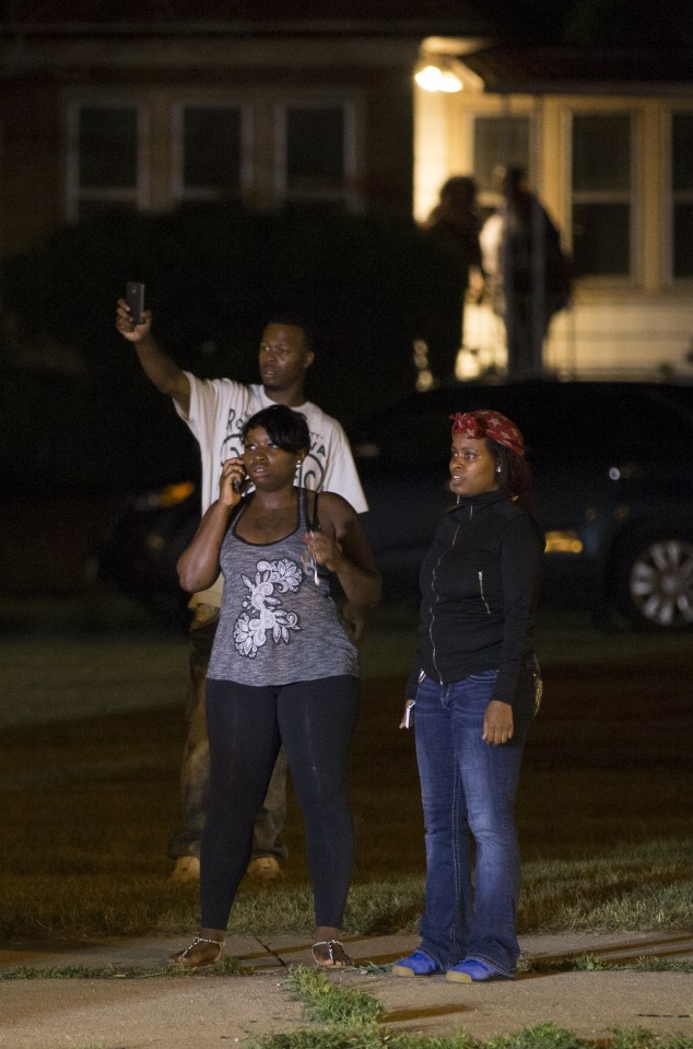  Bystanders watch as a crowd of more than 100 people gathers following the fatal shooting