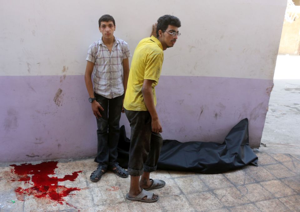  Syrian men stand next to a body bag in front of a makeshift hospital in the Tariq al-Bab neighbourhood of Aleppo, following reported air raids that targeted rebel-held areas in the northern city on August 16