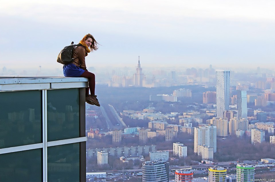 The 23-year-old dangles her legs over the edge of a building with the massive drop just below