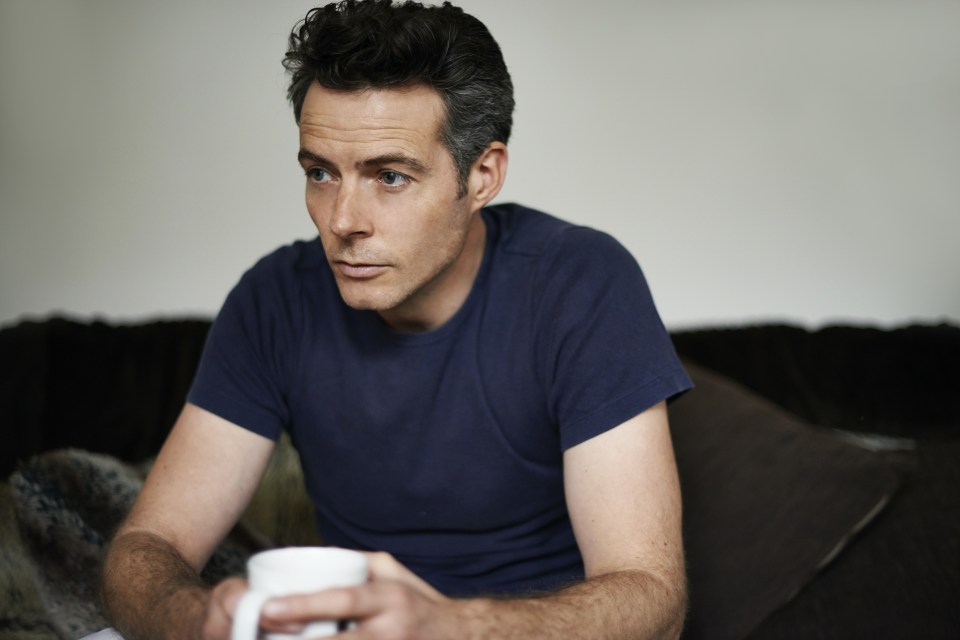 Man sitting on sofa holding mug looking sad