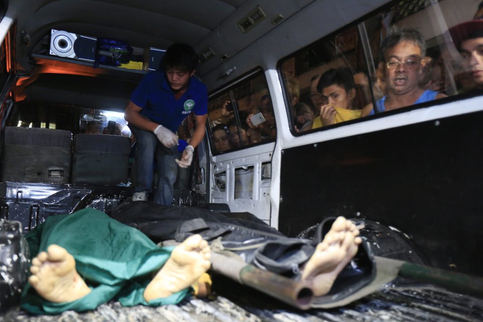  Filipinos peer through the window of a morgue van that is driving away the body of two drug dealers who have been shot dead