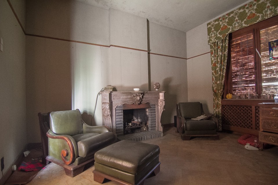 The living room contains dust-covered leather sofas next to an old wooden fireplace