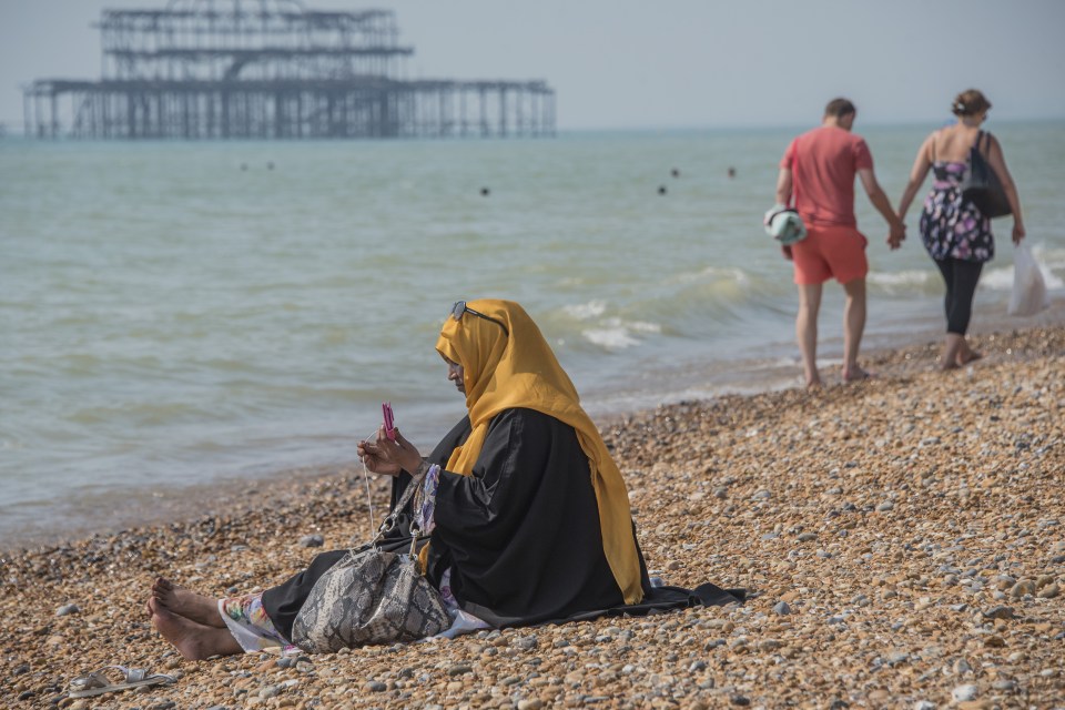  A mother, in a hijab, watches over her family who are also modestly dressed, as they play in the sea on Brighton Beach