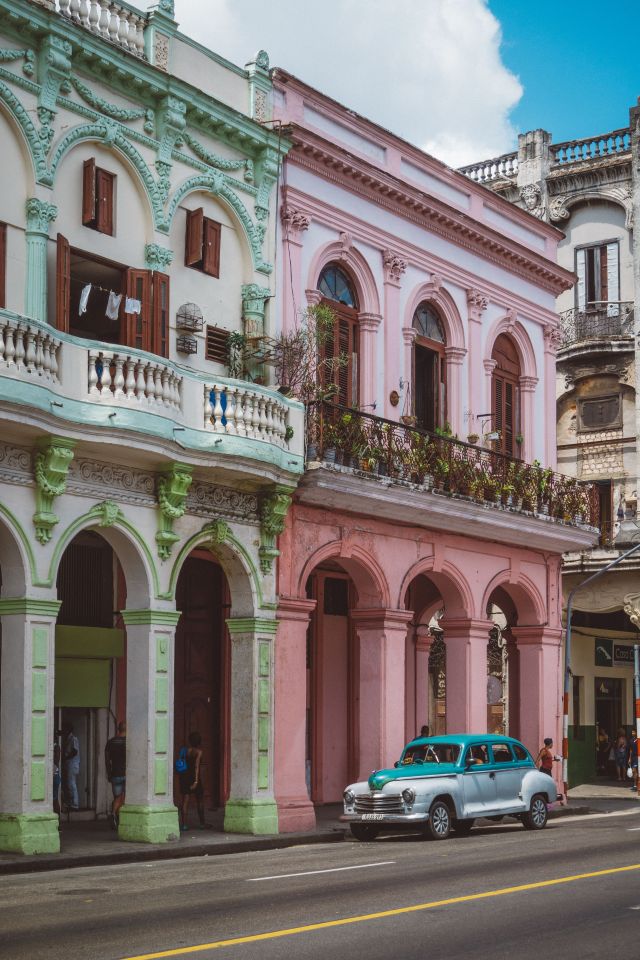 A mint and blue coloured vintage car parked beside Havana's equally colourful houses 