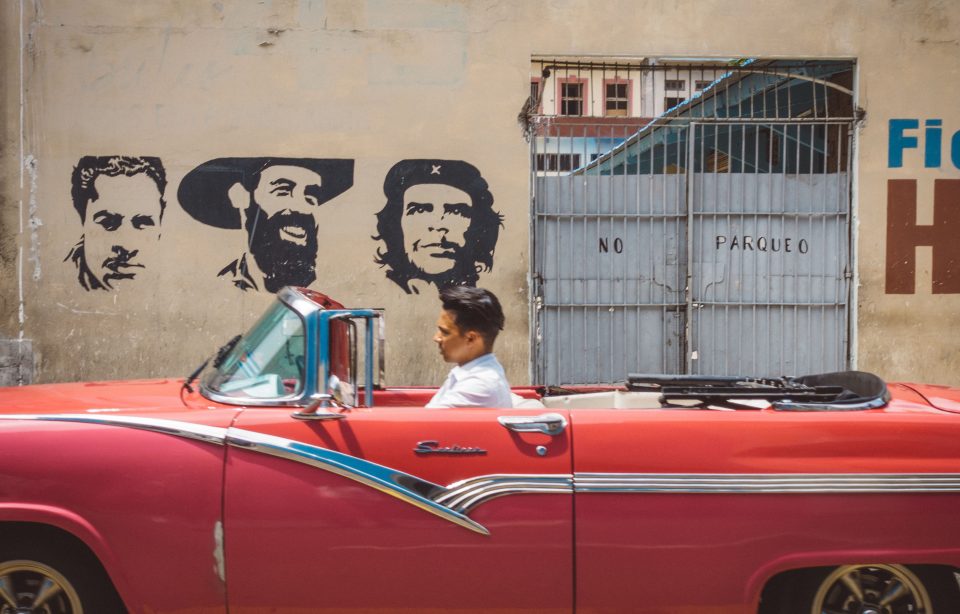 A vibrant red car drives past graffiti showing commie heroes Fidel Castro and Che Guevara 