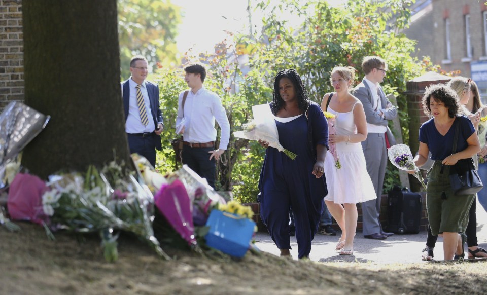 A woman stands over the horror crash site holding a bouquet of flowers