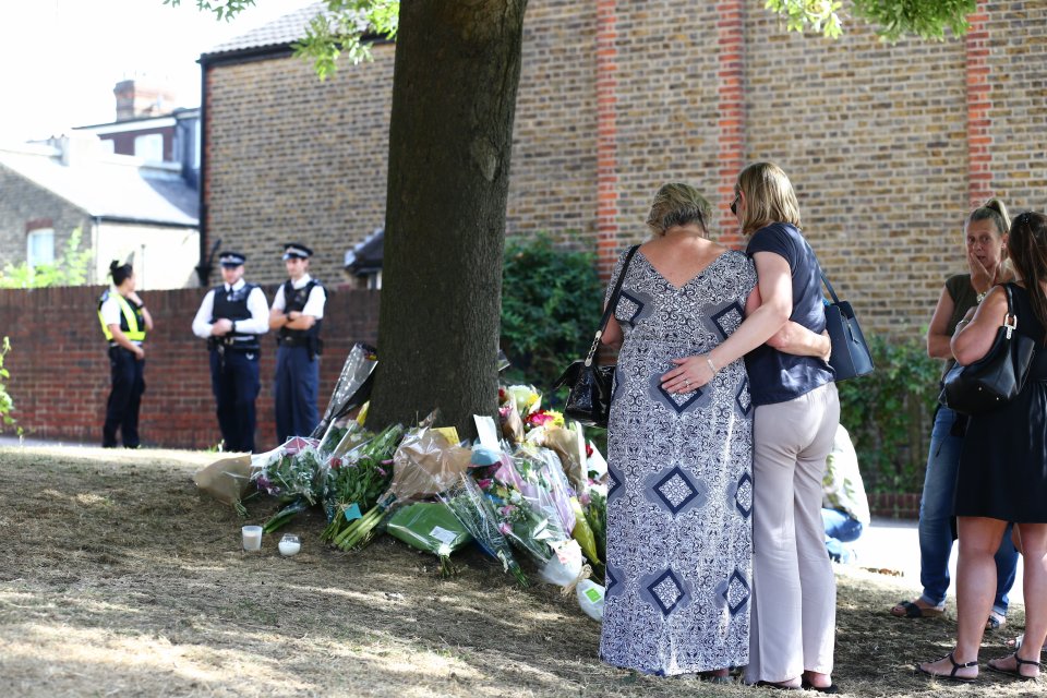 Two women look at the tributes which massed at the site today