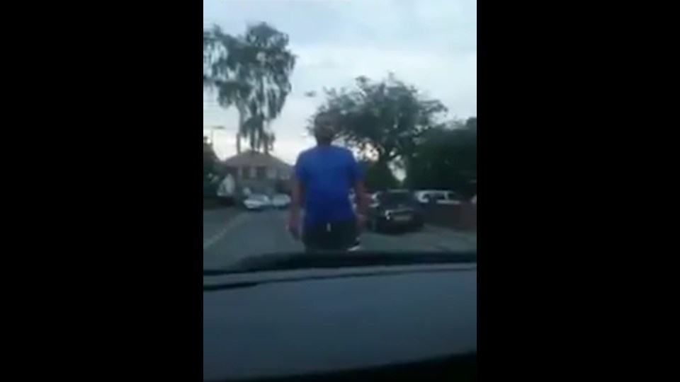 A man can be seen standing in front of the car, blocking the motorist from driving away