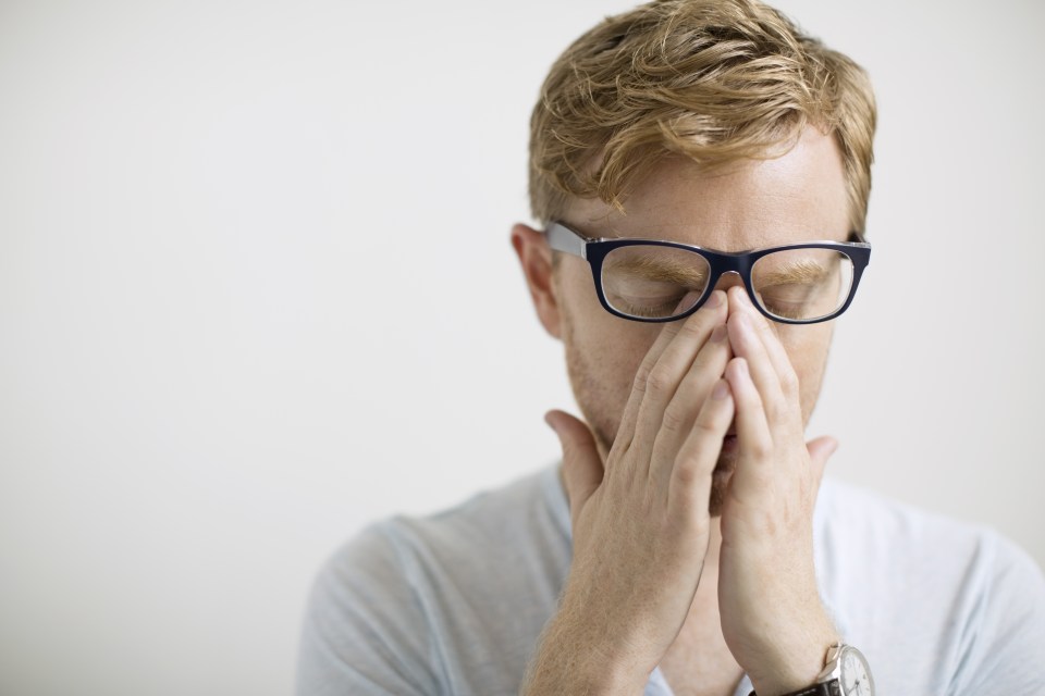 Blonde man rubbing eyes under eyeglasses