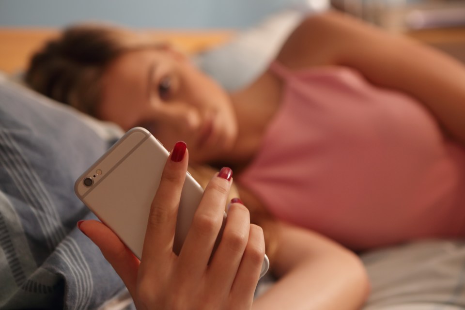 Young woman laying on bed looking at phone