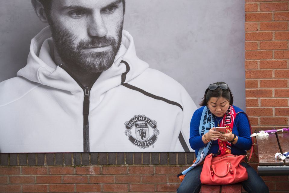 A fan uses a mobile phone ahead of the derby behind a mural of Juan Mata