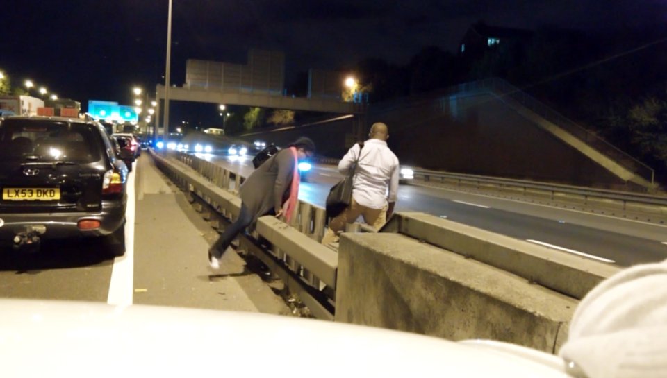 The woman struggles to get over the first barrier with the pair standing next to the M25 for several moments before making the dash to the other side