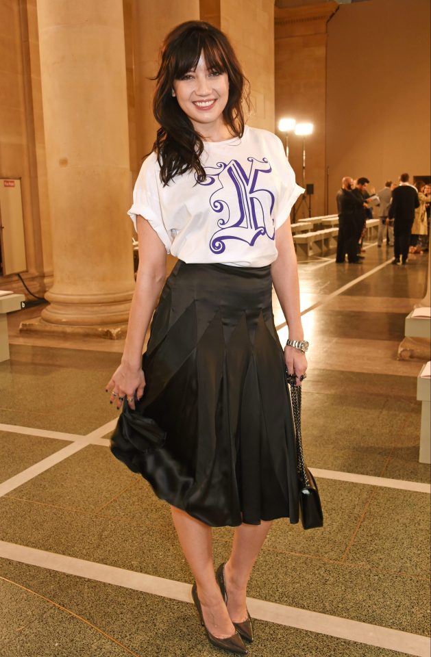 Daisy wore a white top with a large letter K branded across the front with a pleated black skirt