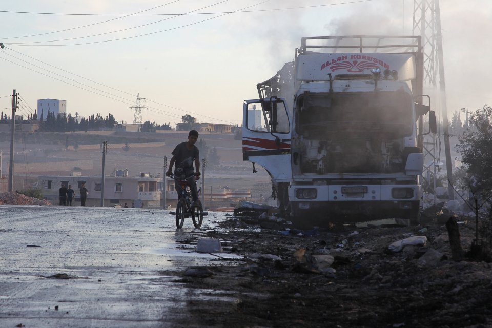  A boy rides a bicycle near a damaged aid truck