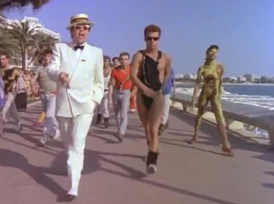  A scantily=clad Bruno marches next to Elton in the video