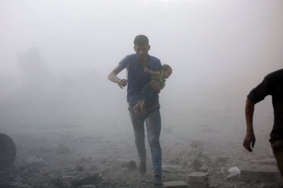 A Syrian man carrying a child emerges fr