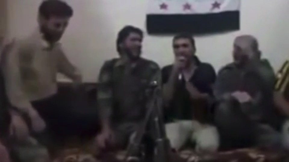 A man comes to sit with the other Free Syria Army members, with the group singing into a microphone