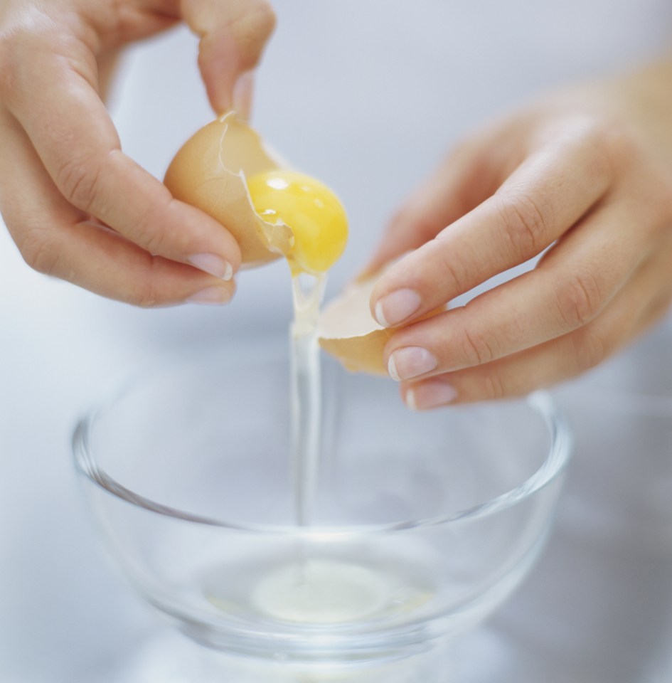 Cracked raw egg being separated over glass bowl, close up