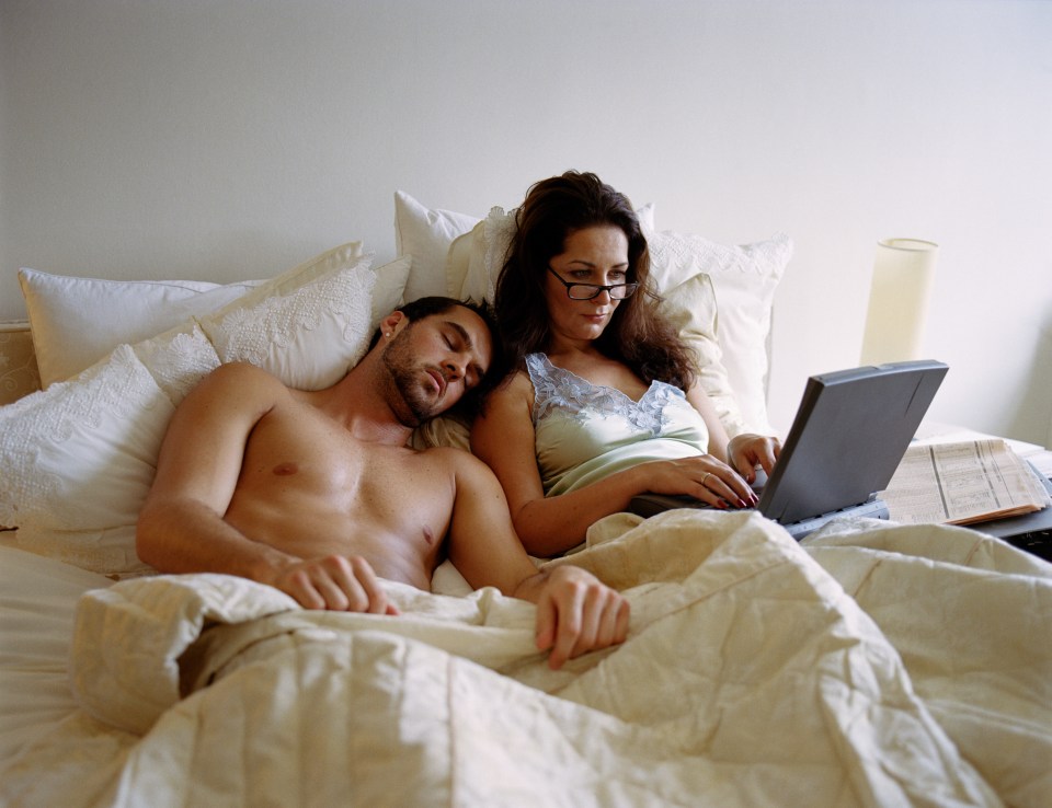 Young man and mature woman in bed, woman using laptop