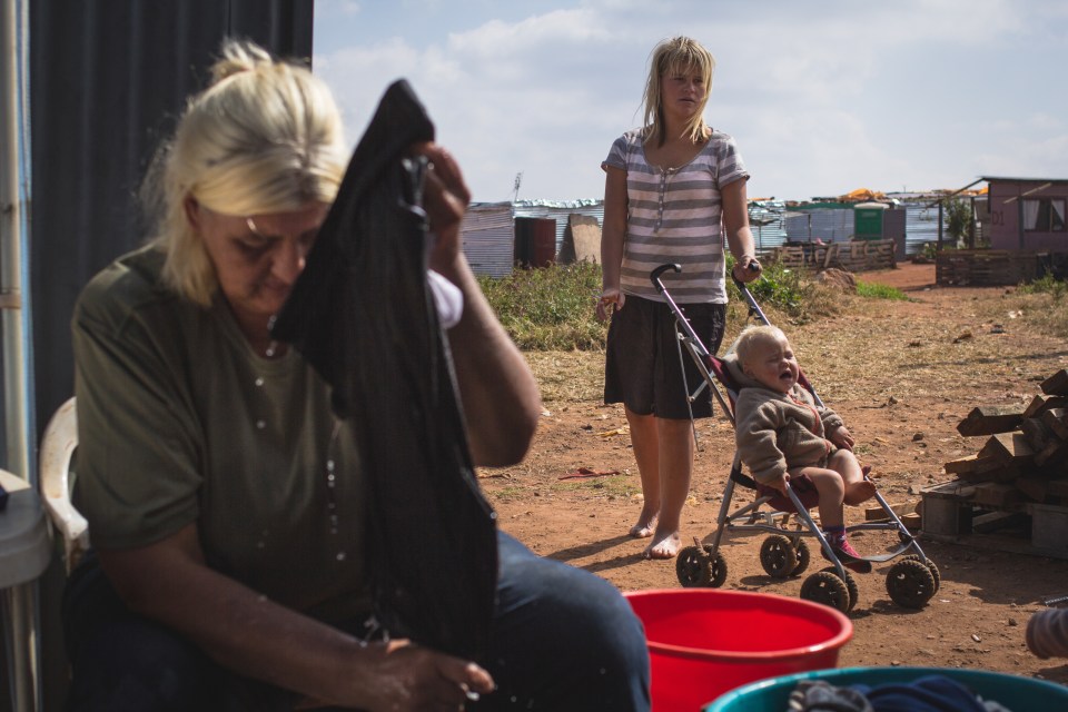  Irene Van Niekerk washes her clothes in a bucket as her daughter tries to calm down her crying grandson in the background