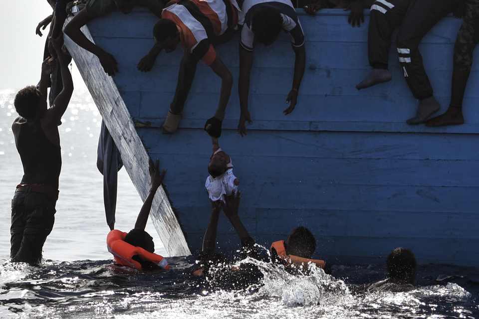 Migrants try to pull a child out of the water as they wait to be rescued