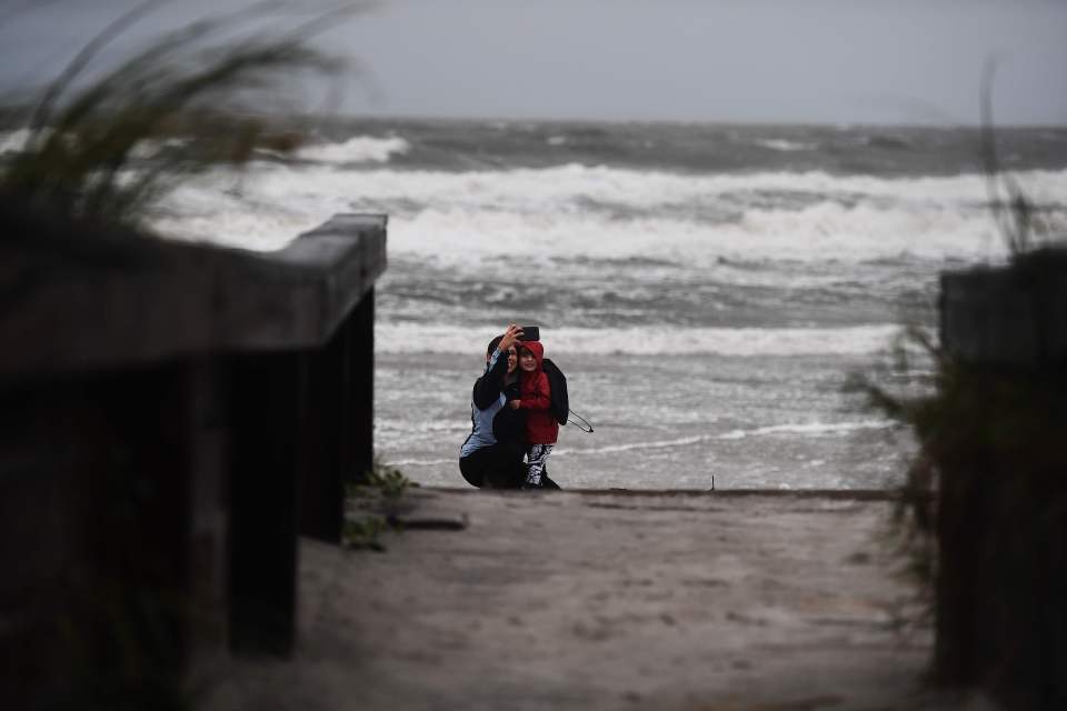 A woman and her daughter take pictures at Neptune Beach, where violent sea swells show the off-shore effect of the storm