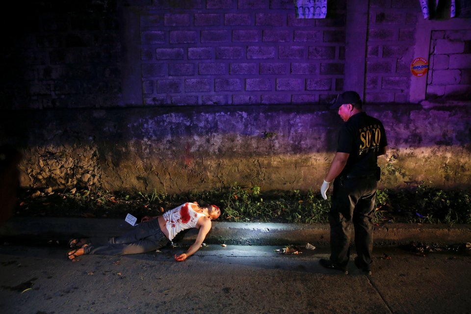 A policemen inspects the scene of the body of a man, who police said was a drug dealer shot dead during a drug buy-bust operation, along a street in Quezon city, Metro Manila