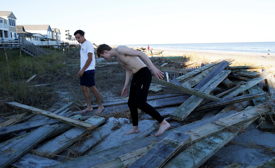 People look around the debris of the pier damaged by Hurricane Matthew in Surfside Beach