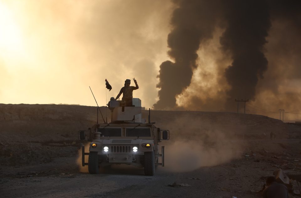 Iraqi army forces look out across a village where smoke rises from oil wells set on fire by ISIS