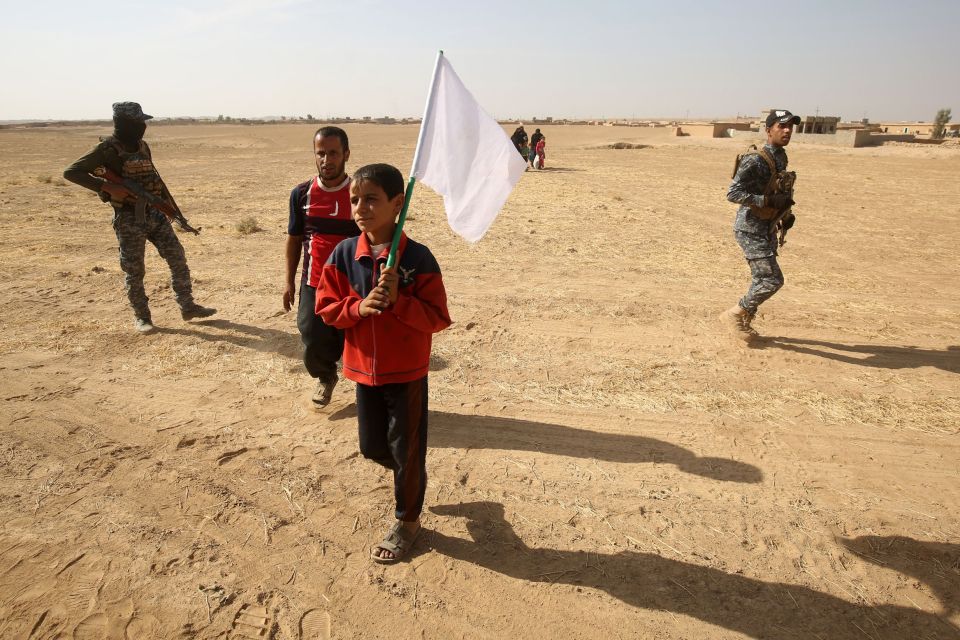 A young refugee boy waves the white flag of surrender after the village of Bajwaniyah is liberated