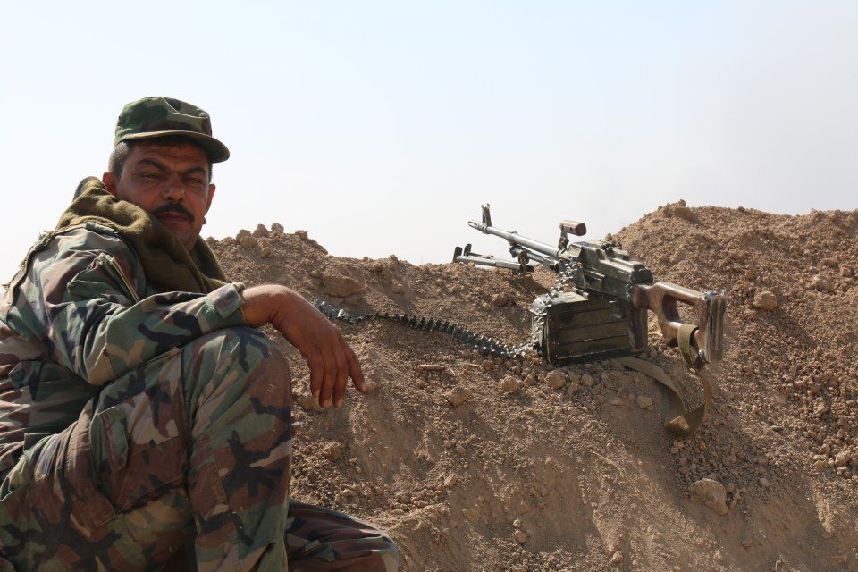 A Kurdish fighter poses next to his machine gun while holding a defensive position