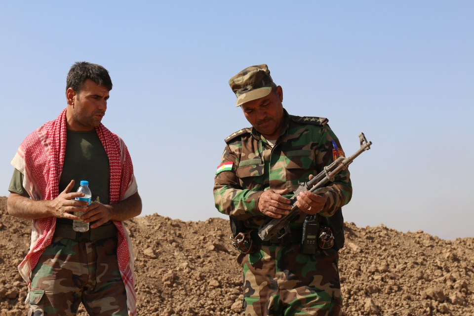 Two Kurdish fighters - who are working with Iraqi troops to liberate Mosul - stand at the scene of last night's skirmish